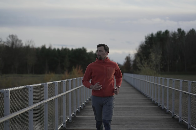 Cross country jogging in countryside man in orange sweatshirt running across wooden bridge in