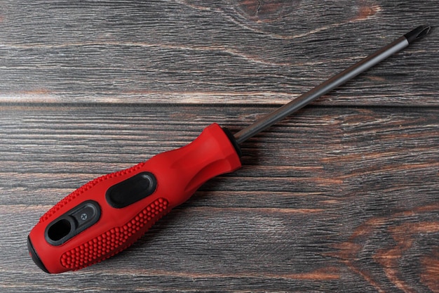 Cross screwdriver with red handle on wooden background