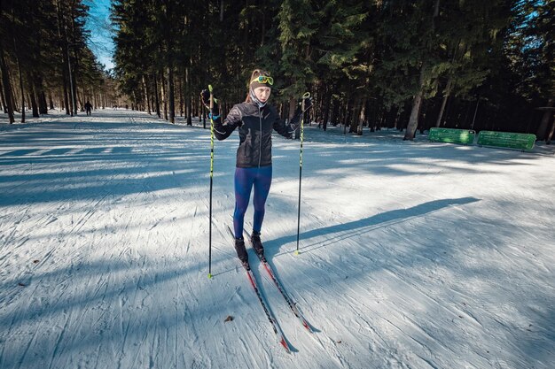 写真 雪に覆われた森のトレイルトラックで古典的な北欧のクロスカントリースキーをしているクロスカントリースキーの女性モスクワオジンツォボの公園でスキーヤーのためのトレーニングトラック