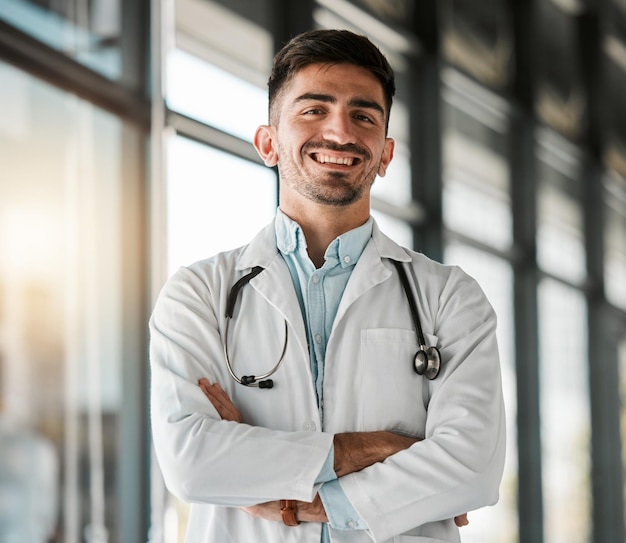 Photo crossed arms confidence and portrait of a male doctor with a stethoscope in a medical hospital happy smile and headshot of a professional young man healthcare worker or surgeon in medicare clinic