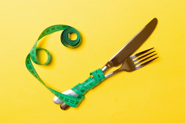 Crossed fork and knife are wrapped in measuring tape