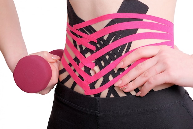 Crossed kinesio tape on abdomen of girl with dumbbell in her hand.