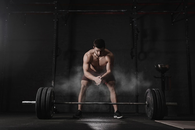 写真 crossfit アスリートが手を叩き、ジムで重量挙げの準備をする バーベル マグネシア保護ダスト クラウド 機能トレーニングを行うハンサムな男性 パワーリフティングの練習 トレーニング演習