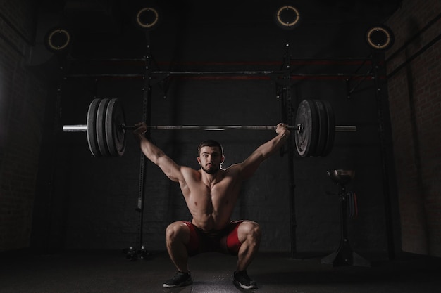 Foto atleta crossfit che solleva pesante bilanciere sopra la testa in palestra praticando il powerlifting