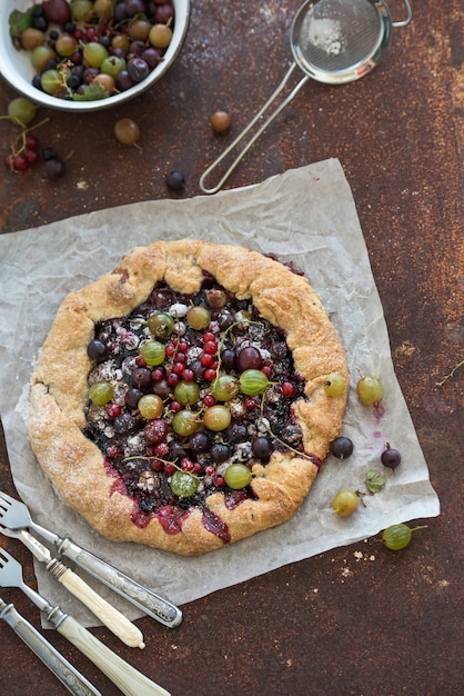 Crostata or galette pie with fresh garden berries over grunge rusty metal surface, top view