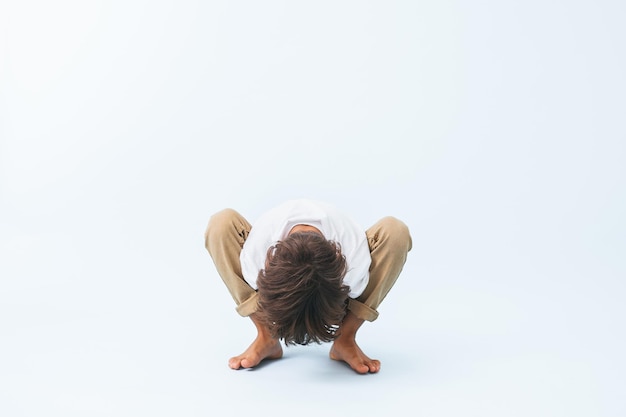 Crouching Indian boy lowering his body betweeen legs against bluish white