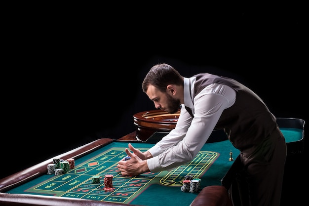 Croupier achter goktafel in een casino op een zwarte achtergrond. Gokken. Casino. Roulette. Poker