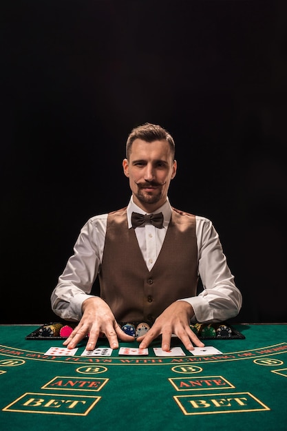 Croupier behind gambling table in a casino on black background. The concept of victory.