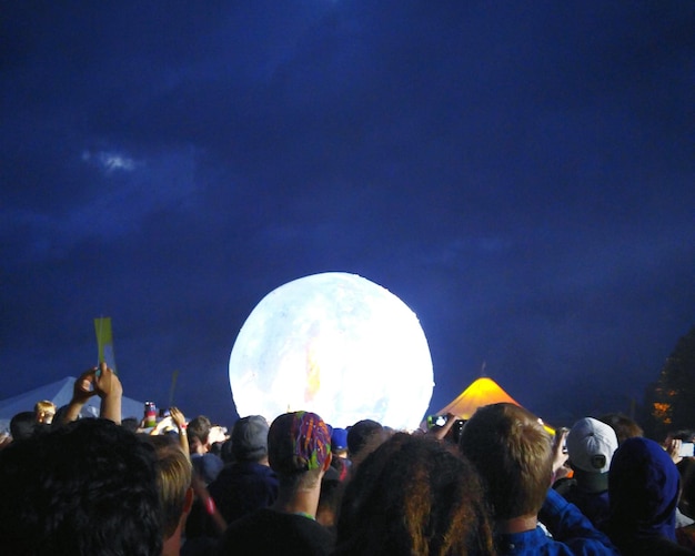 Photo crowd enjoying at music concert against moon in sky at night