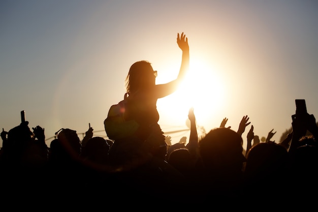 Photo the crowd enjoys the summer music festival, sunset, the black silhouettes hands up, girl in the center