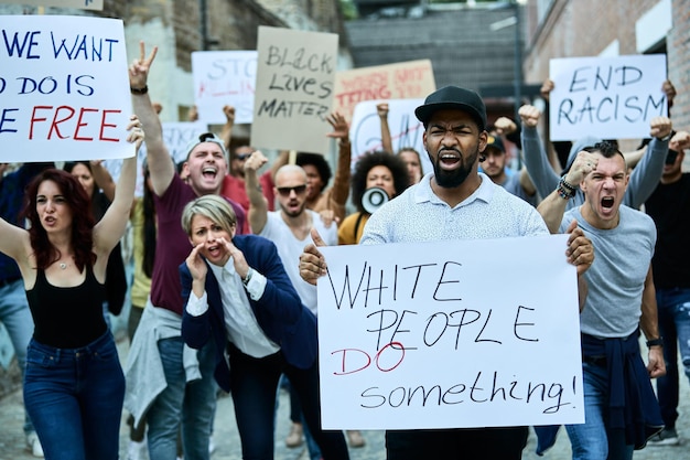 Crowd of people protesting against racism on city streets Focus is on black man holding banner with 'white people do something' inscription