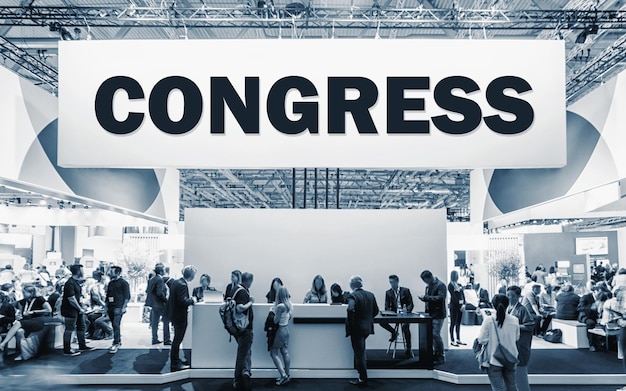 Photo crowd of people at a trade show booth with a banner and the text congress