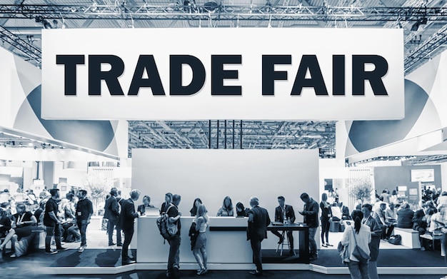 Photo crowd of people at a trade show booth with a banner and the text trade fair