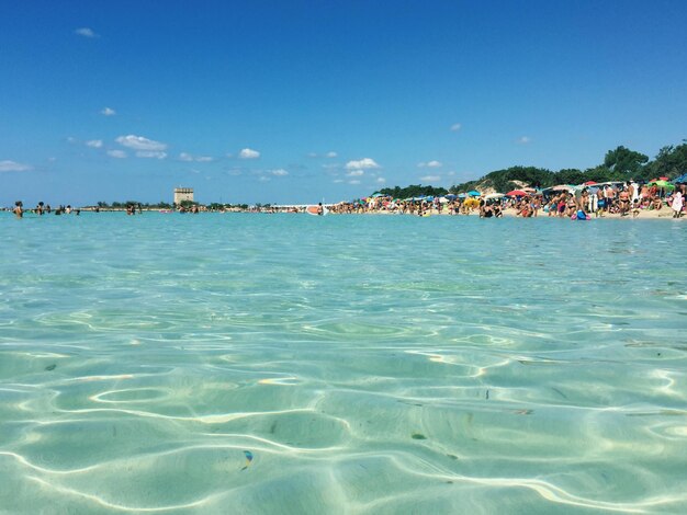 Crowd at sea shore against blue sky