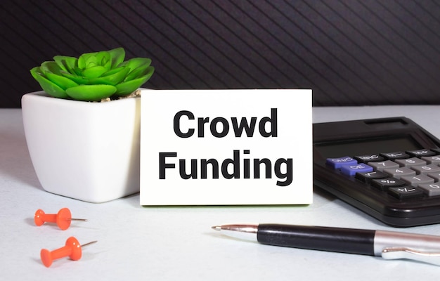 Crowdfunding Een gouden spaargeldkaart en rekenmachine op houten achtergrond met tekst Crowd Funding