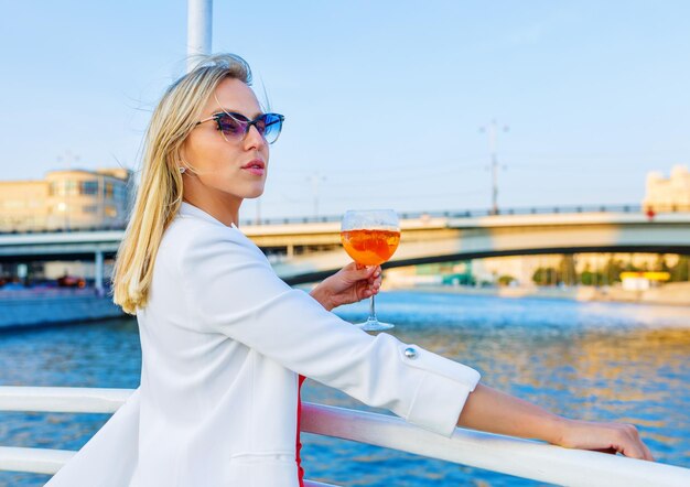 Cruise boat vacation young pretty woman in sunglasses relaxing\
on deck enjoying view from boat drinks cocktail aperol syringe\
happy casual tourist girl on holiday destination