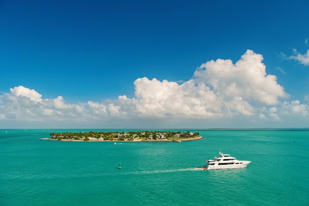 cruise toeristische boten of jachten drijvend per eiland met huizen en groene bomen op turquoise water en blauwe bewolkte hemel, zeilen en eilandleven rond het prachtige Key West Florida, VS