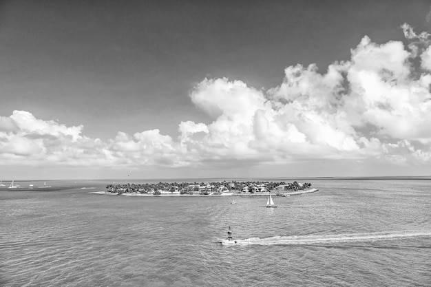 Cruise touristic boats or yacht floating by island with houses\
and green trees on turquoise water and blue cloudy sky yachting and\
isle life around beautiful key west florida usa