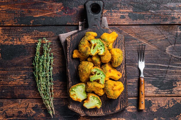 Crumbed broccoli steaks on a wooden board. Dark wooden background. Top view.