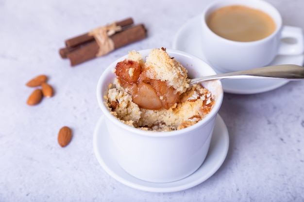 Crumble with caramelized pear, cinnamon and almonds in a white ramekin. Close-up.