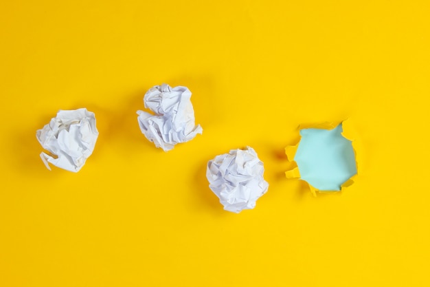 Crumpled balls of paper, a torn hole in yellow paper. Top view. Minimalistic business concept