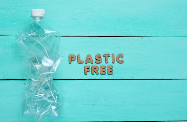  Crumpled bottle on a blue wooden surface with text plastic free