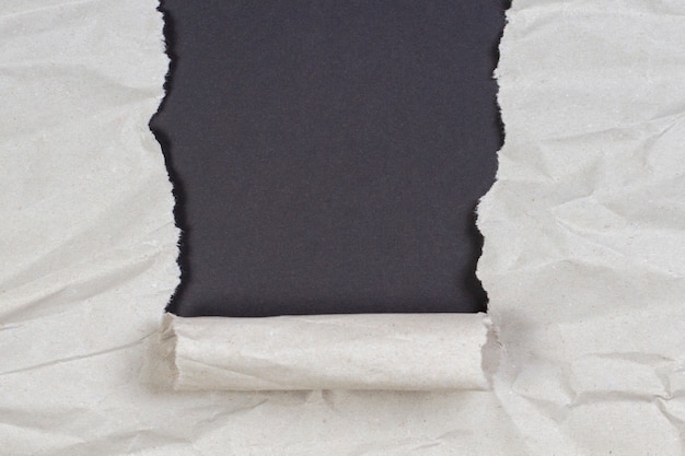 Crumpled package paper torn to reveal black wall with copy\
space