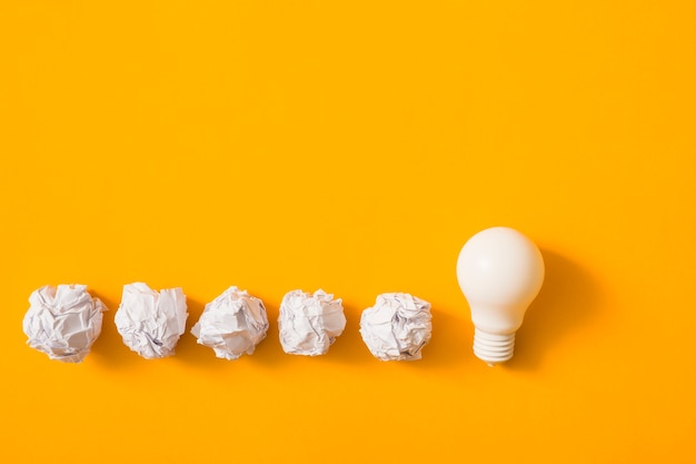 Crumpled paper ball with white light bulb on yellow background