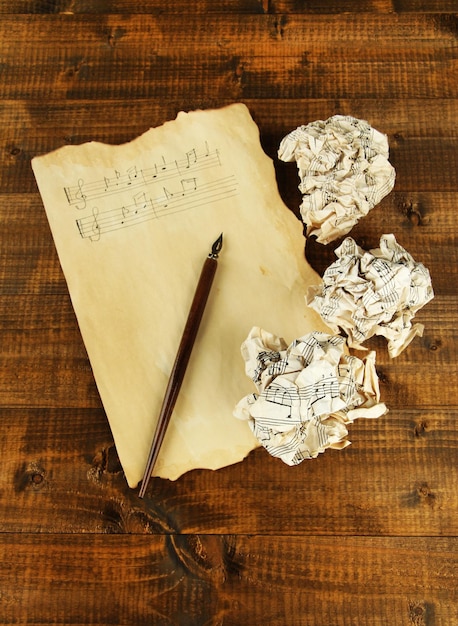 Crumpled paper balls with ink pen and music sheet on wooden background