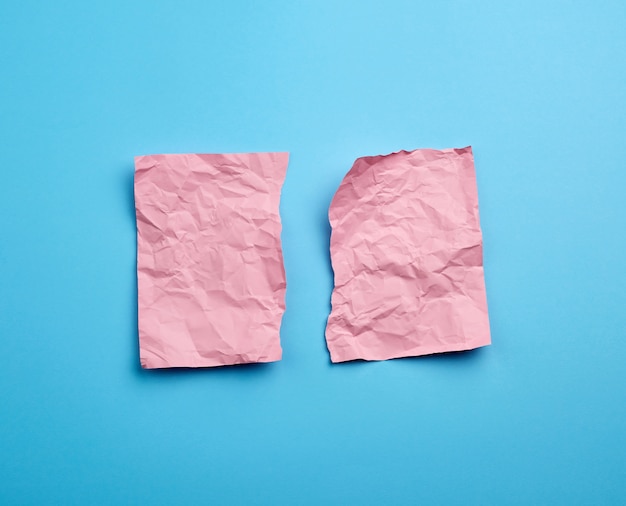 Crumpled pink sheet of paper torn in two on a blue 