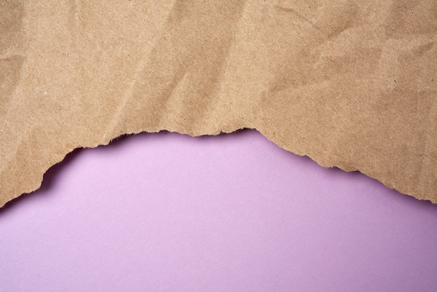 Crumpled sheet of brown wrapping paper with torn edges on a purple background