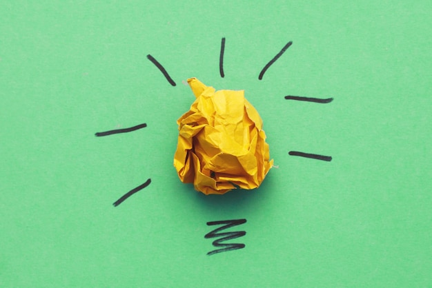 Мятая желтая бумажная лампочка как концептуальная творческая идея и инновации на зеленом фоне