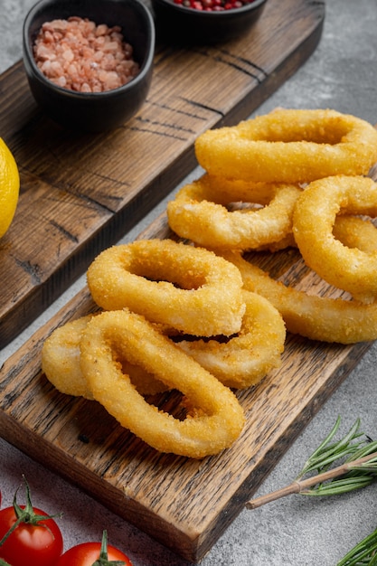 Crunchy deep fried squid or onion rings in batter set, on serving board, on gray stone table background