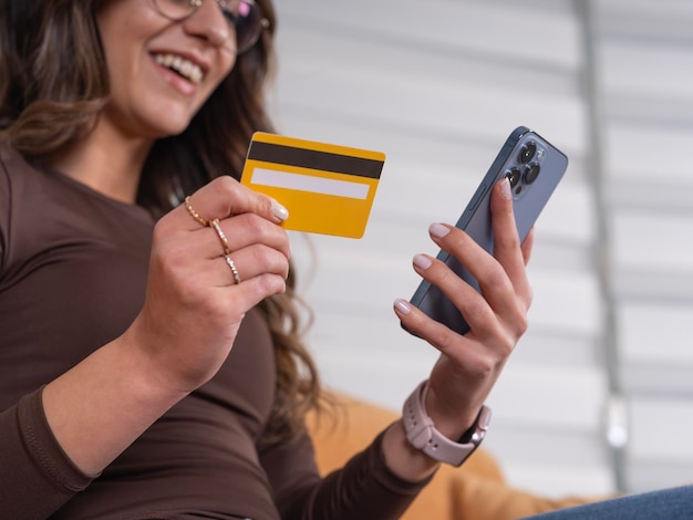 crunette happy woman holding smartphone and credit card online mobile shopping at home