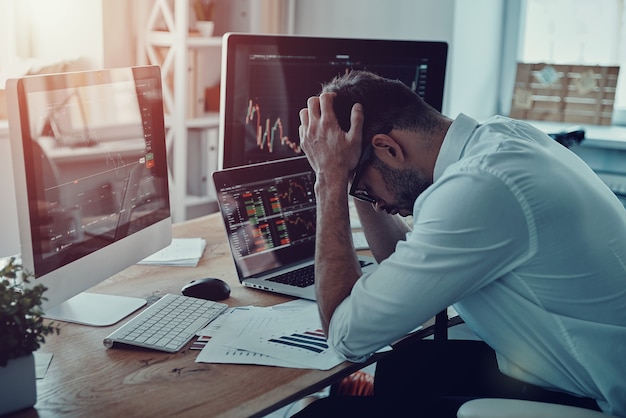 Crush! Frustrated young businessman in formalwear keeping head in hands while sitting in the office