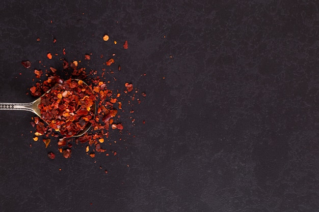 Crushed dried chili peppers in an iron spoon scattered on a black . , copyspace.