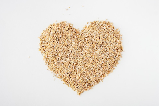 Crushed oats are scattered on a white background in the shape of a heart copy space