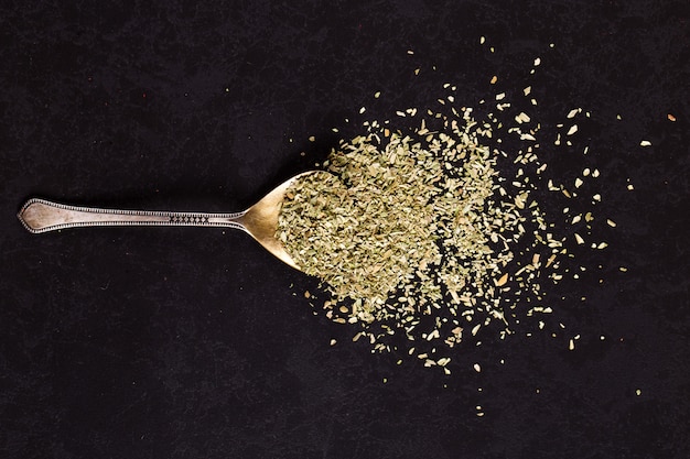 Crushed oregano scattered in an iron spoon on a black table. , copyspace.