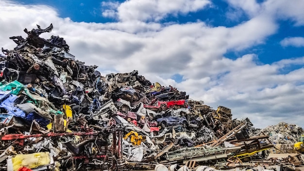 Photo crushed vehicles at a scrap yard against blue cloudy sky