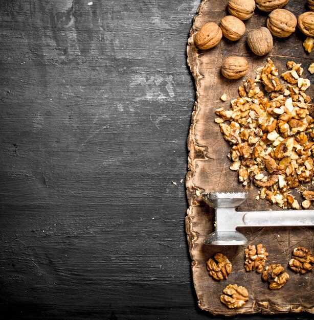 Crushed walnuts with a hammer on old Board on black chalkboard