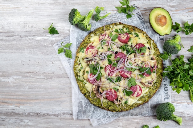 Photo crust broccoli base low carbs keto pizza with salami avocado on vintage newspapper top view