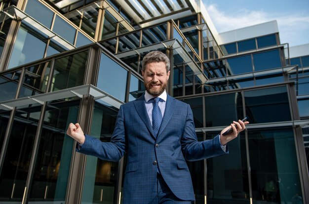 Crying bearded businessman in formal suit with smartphone\
bankruptcy