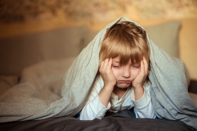 crying boy under the blanket on the bed