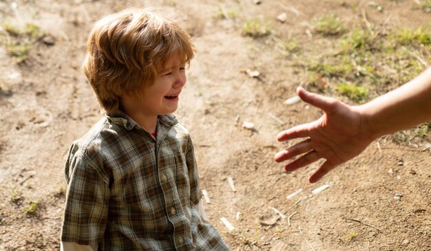 Crying capricious boy is sitting on the road, father provides hand. Parent Helping Hands.