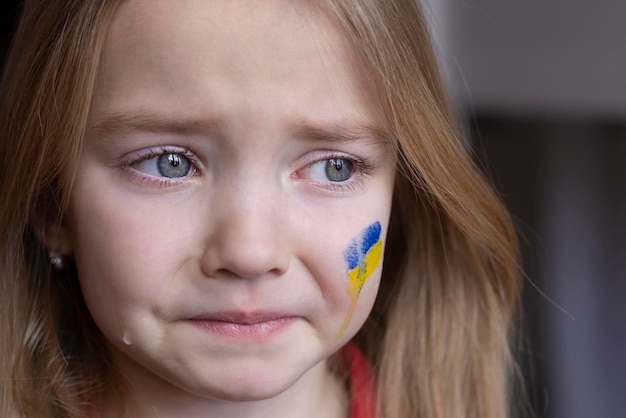 A crying child flowing tears a Ukrainian flag on her cheek children want peace