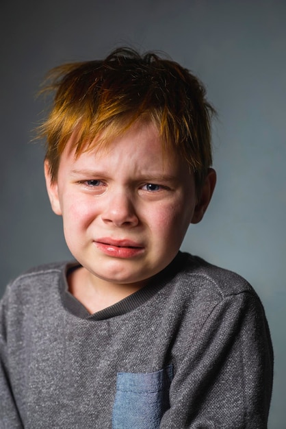 Ragazzo di otto anni che piange su uno sfondo grigio