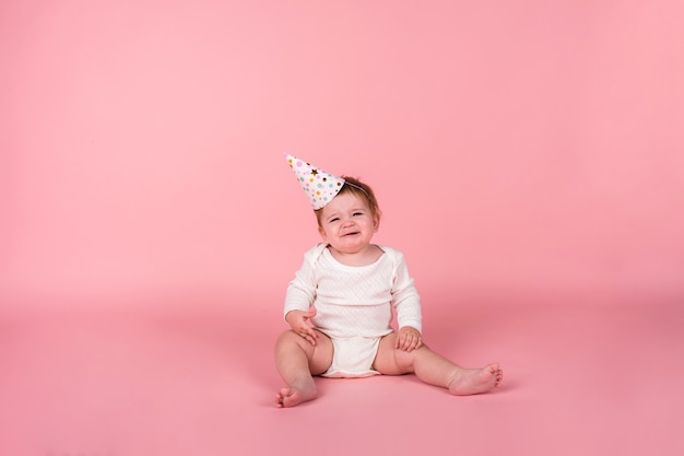 A crying girl in a white bodysuit and a holiday hat