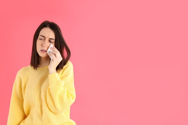 Crying girl in yellow sweater on pink background