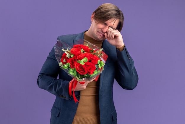 Crying handsome slavic man holding gift box and bouquet of flowers on valentine's day 