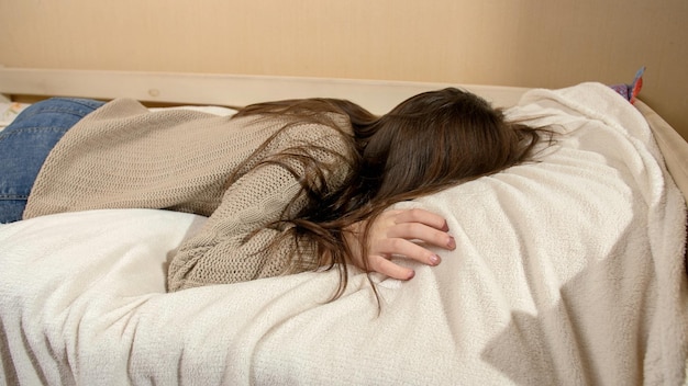 Photo crying teenage girl jumping on bed and lying on soft pillow